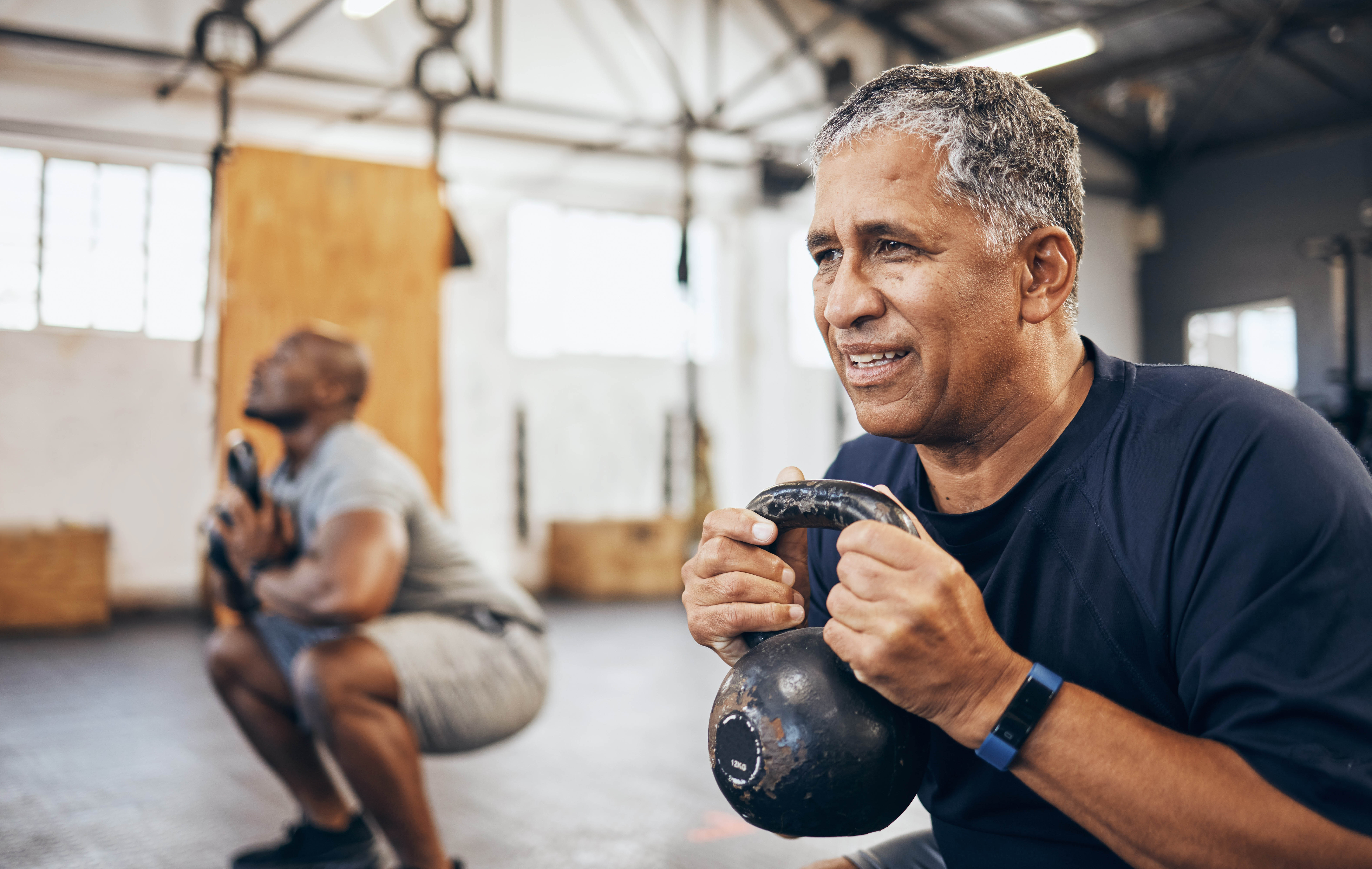 Aging man struggling to complete kettlebell squats in a workout class at the gym Aging man struggling to complete kettlebell squats in a workout class at the gym